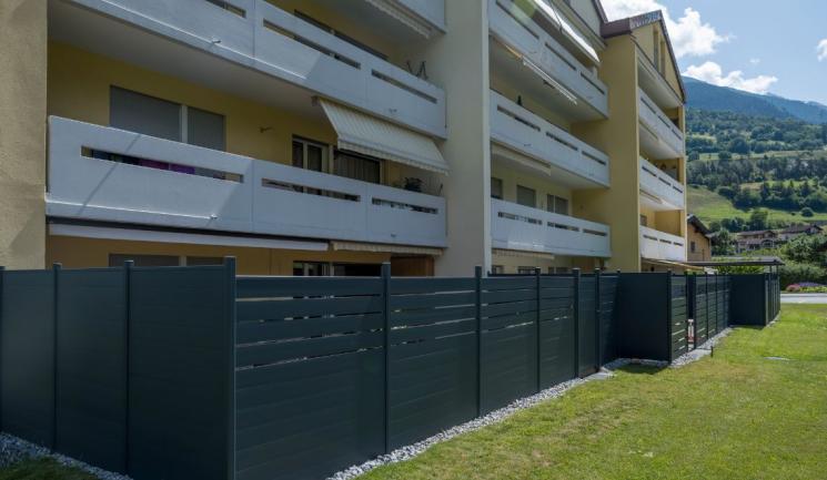 Clôture composite anthracite Silvadec pour aménagement extérieur résidentiel - Occultation de jardin en bois composite installée en alignement devant immeuble collectif